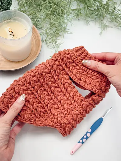 Hands holding a rust Wheat Stitch Crochet Dog Sweater with a crochet hook