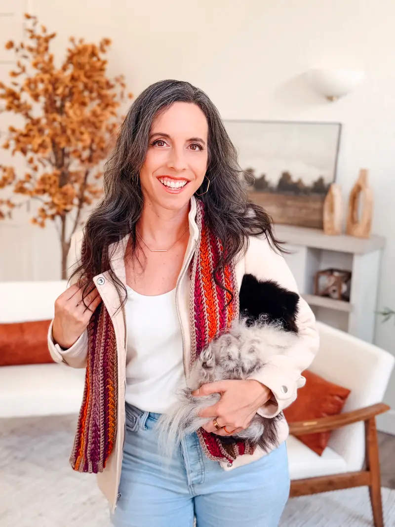 Woman wearing a striped Wheat Stitch Crochet Scarf in red, rust and purple, holding her pomeranian