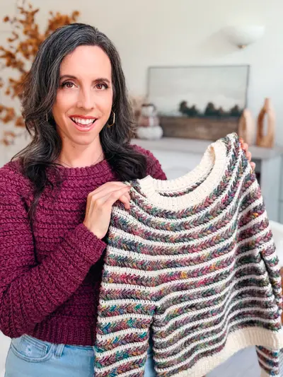 Woman in a burgundy Wheat Stitch Crochet Sweater holding the striped version