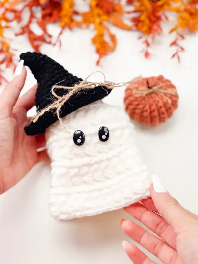 Hand holding a white Wheat Stitch Ghost with a black witch hat