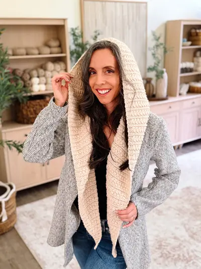 Woman adjusting the hood of the cream Wheat Stitch Hooded Scarf