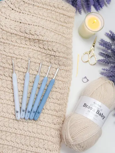 Cream Wheat Stitch Hooded Scarf in progress with crochet hooks and a skein of yarn