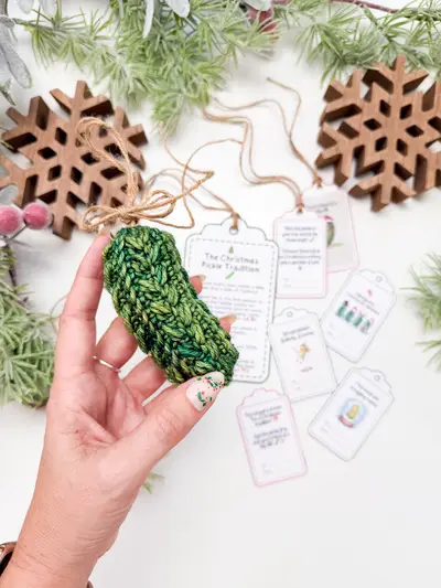 Hand holding a green Wheat Stitch Pickle Ornament with printable tags