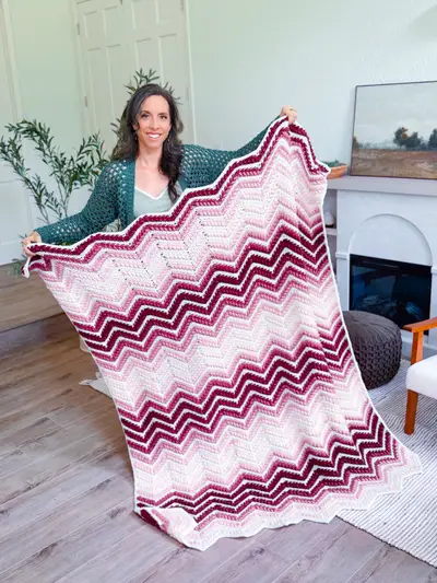 Woman holding up the burgundy and pink Wheat Stitch Ripple Blanket