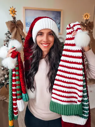 Woman wearing a red Wheat Stitch Santa hat while holding striped elf hats