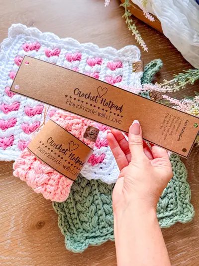Hand holding a Crochet Hotpad gift label over pink and sage hotpads