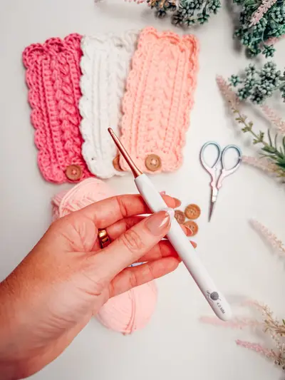 Hand holding a crochet hook beside pink and coral napkin rings