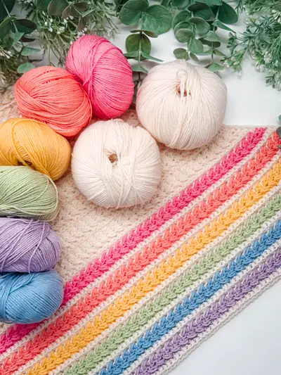 Rainbow skeins of yarn beside the Wheat Stitch Triangle Shawl's striped edge