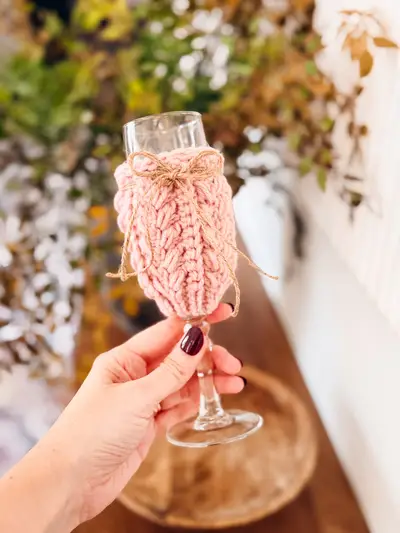 Hand holding a blush Wheat Stitch Wine Glass Cozy on a champagne flute