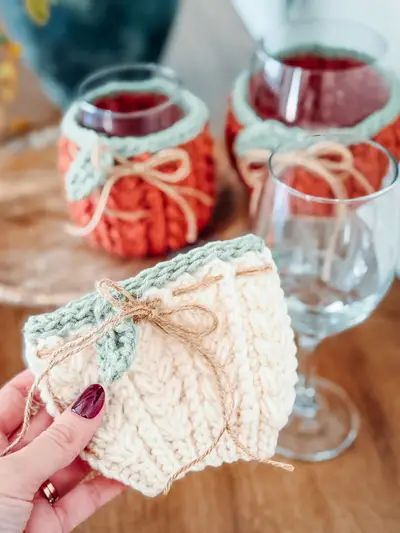 Hand holding a cream Wheat Stitch Wine Glass Cozy with a sage band