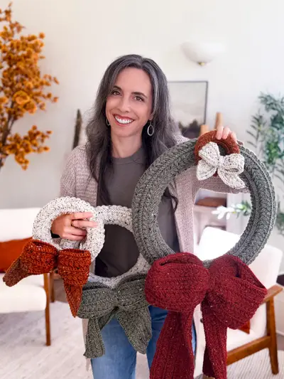 Woman holding three Wheat Stitch Wreaths in cream, sage and gray