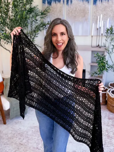 Woman holding up the black Willow Mesh Crochet Wrap to show the lace