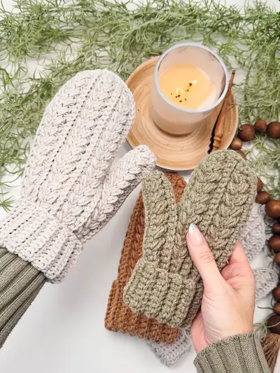 Hand holding a cream Winter Wheat Flat Crochet Mitten beside a candle