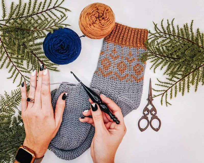 Hands crocheting a Woodland Walker Crochet Sock with blue and tan yarn