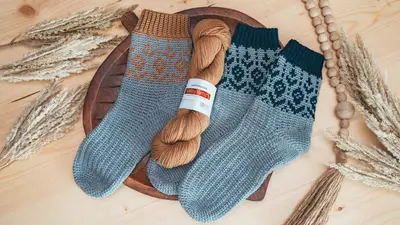 Woodland Walker Crochet Socks in blue and teal with a skein of tan yarn
